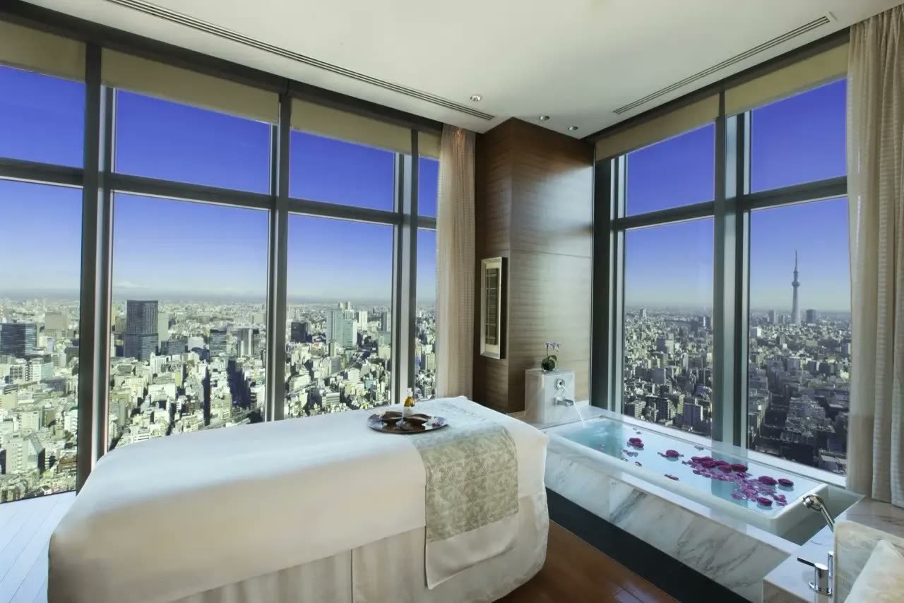 Spa treatment room with floor-to-ceiling city views and a marble bath