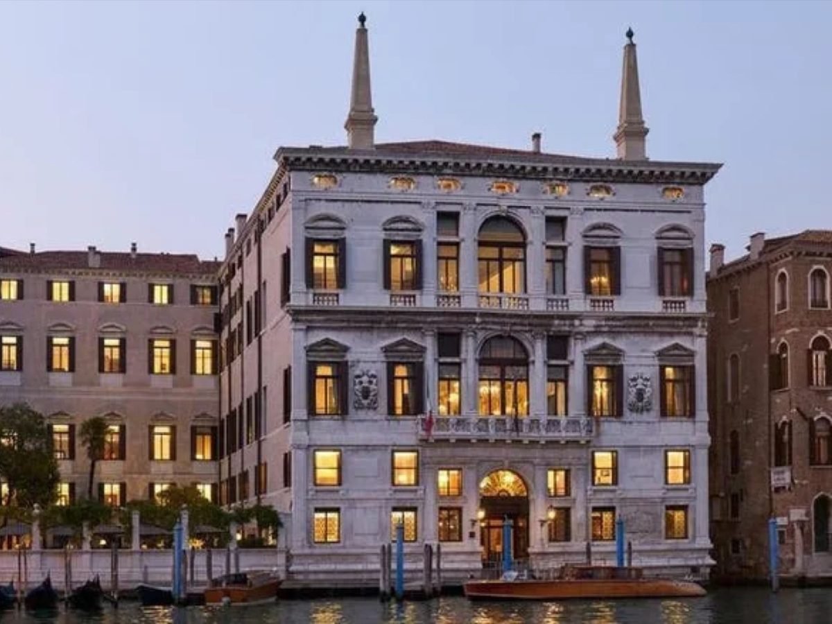 The lit facade of Aman Venice's Palazzo Papadopoli seen from the Grand Canal at dusk