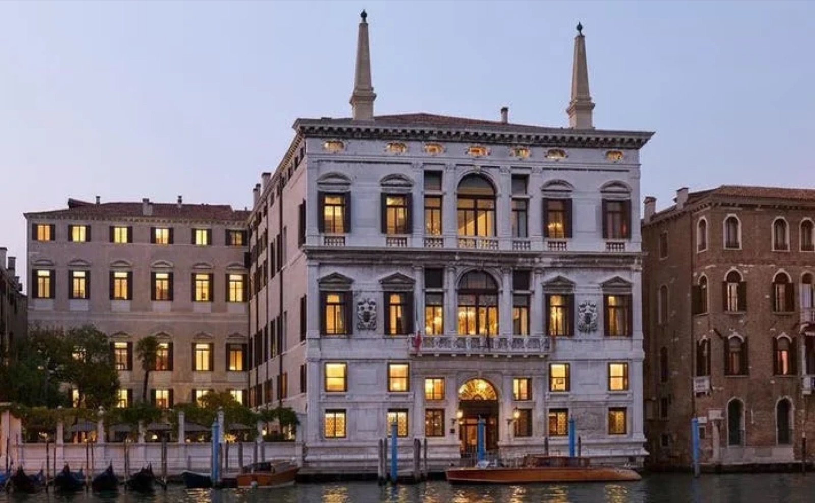 The lit facade of Aman Venice's Palazzo Papadopoli seen from the Grand Canal at dusk