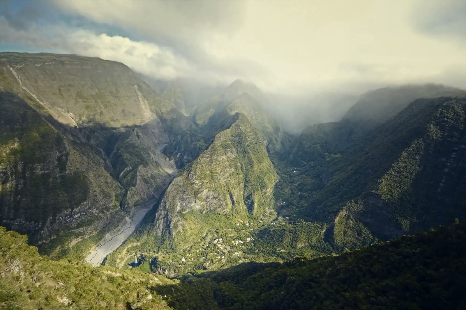 Steep green mountain valley under drifting cloud