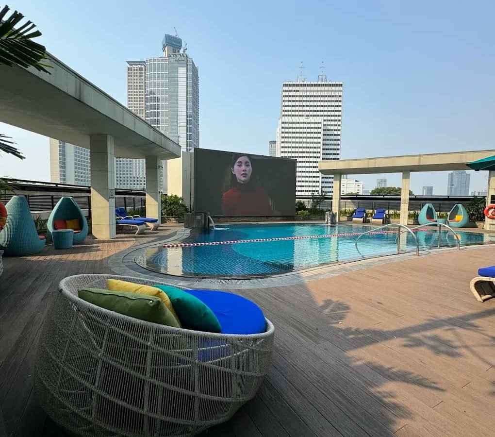 Rooftop pool deck with wicker daybeds and city towers at Mandarin Oriental Jakarta