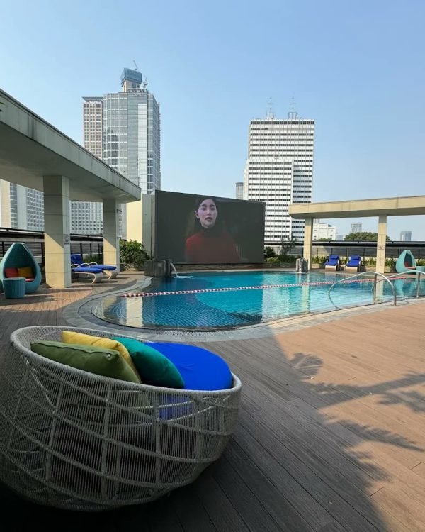Rooftop pool deck with wicker daybeds and city towers at Mandarin Oriental Jakarta