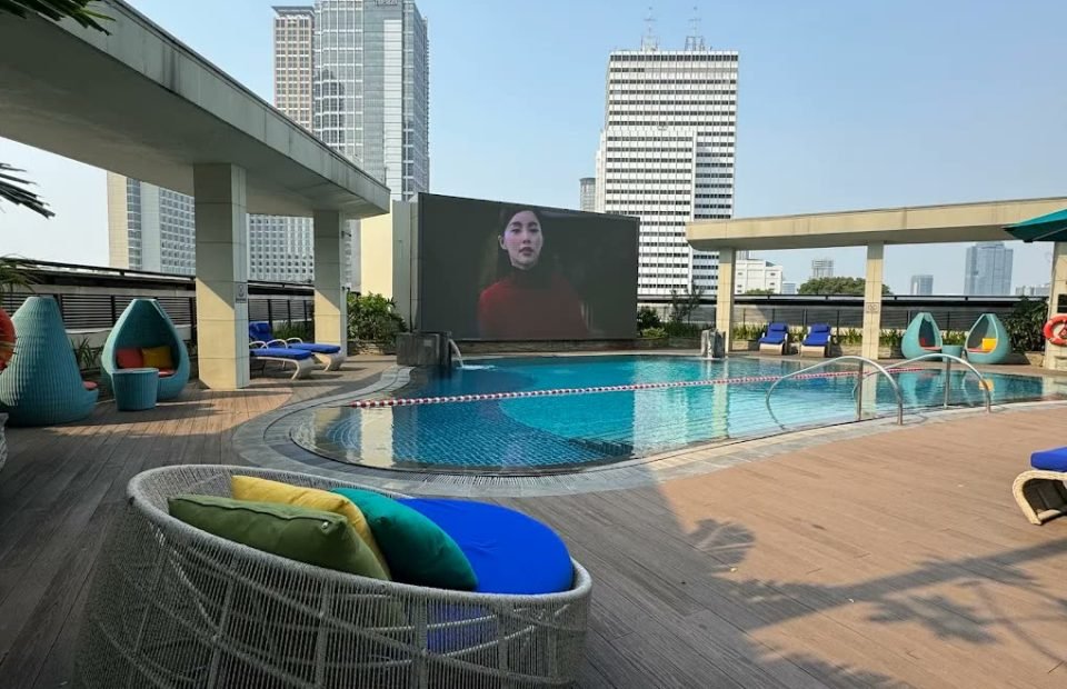 Rooftop pool deck with wicker daybeds and city towers at Mandarin Oriental Jakarta