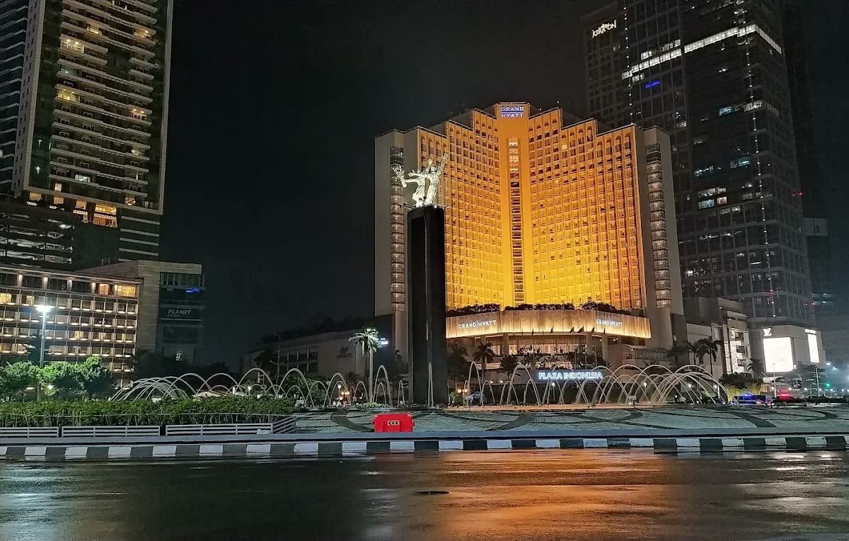 Golden-lit facade of Mandarin Oriental Jakarta seen across the water at night
