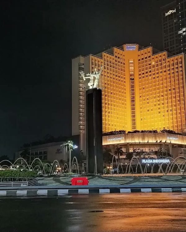 Golden-lit facade of Mandarin Oriental Jakarta seen across the water at night