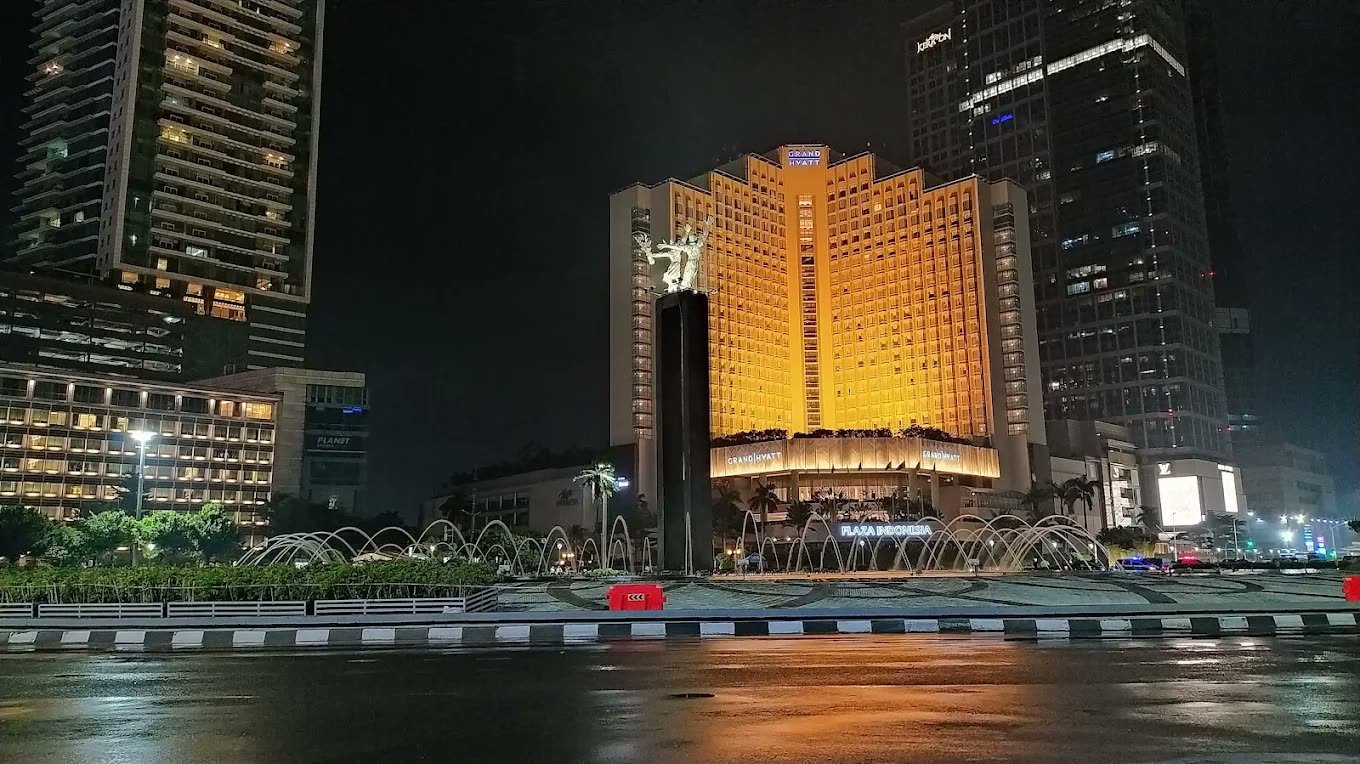 Golden-lit facade of Mandarin Oriental Jakarta seen across the water at night