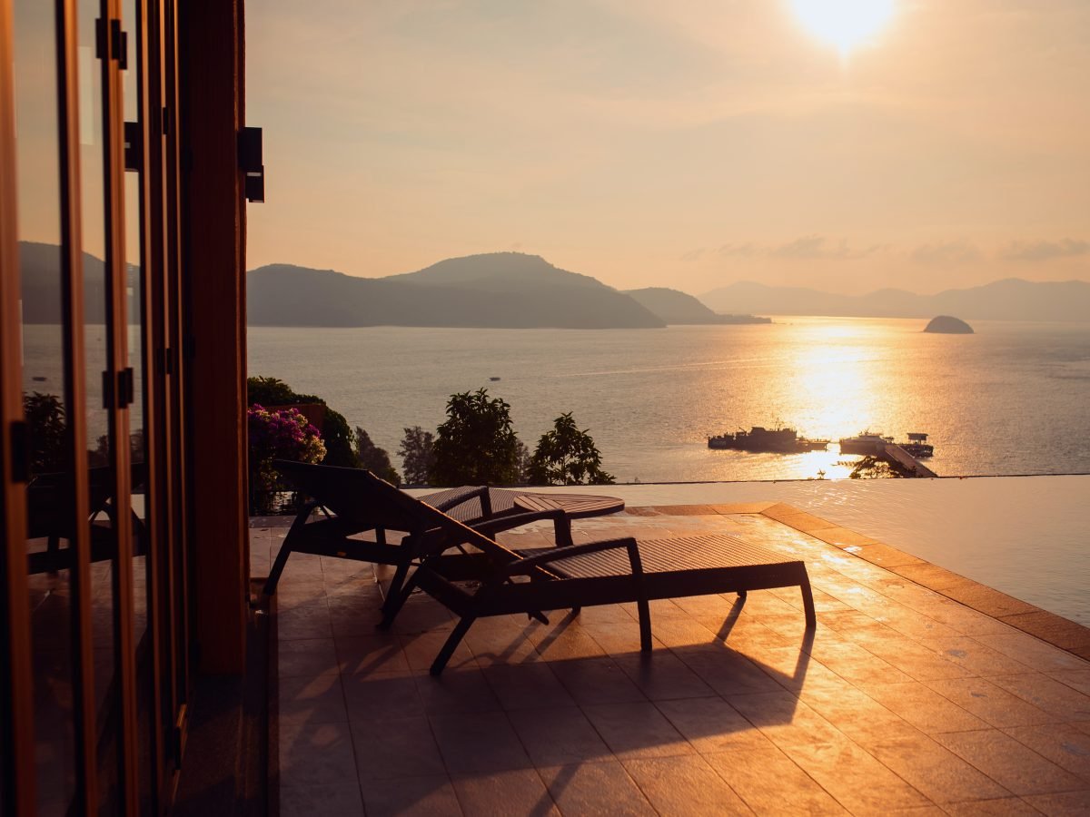 Loungers on a terrace over the sea seen through a suite doorway at golden hour