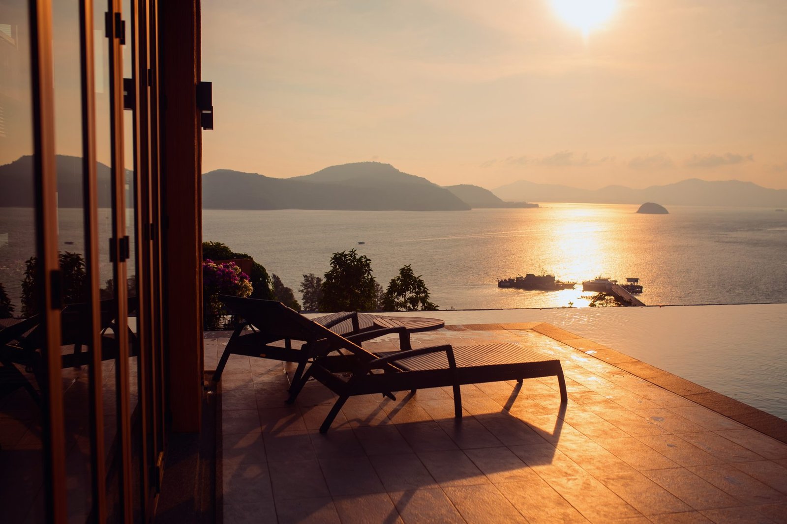 Loungers on a terrace over the sea seen through a suite doorway at golden hour