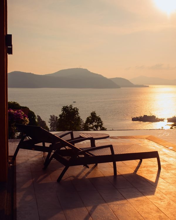Loungers on a terrace over the sea seen through a suite doorway at golden hour