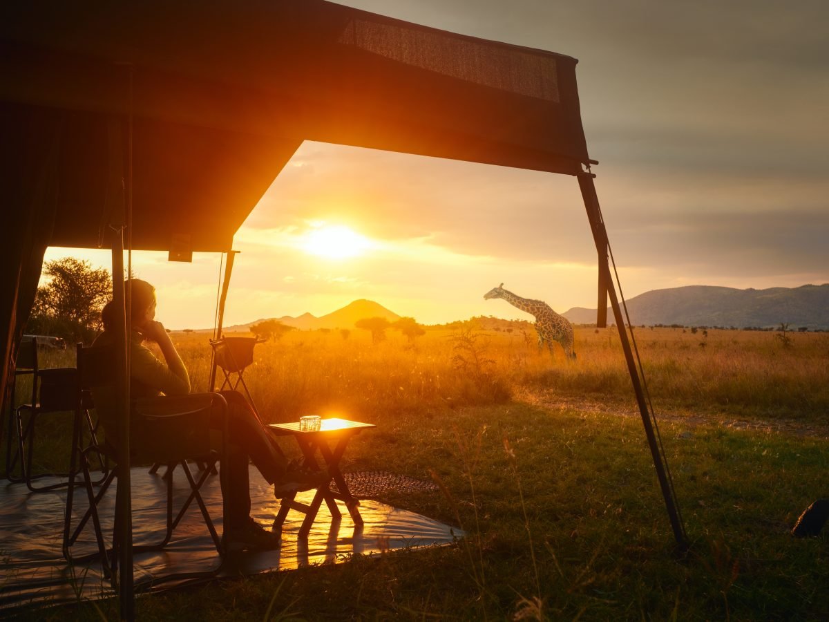 Guest at the edge of a luxury safari tent overlooking the savanna at sunset