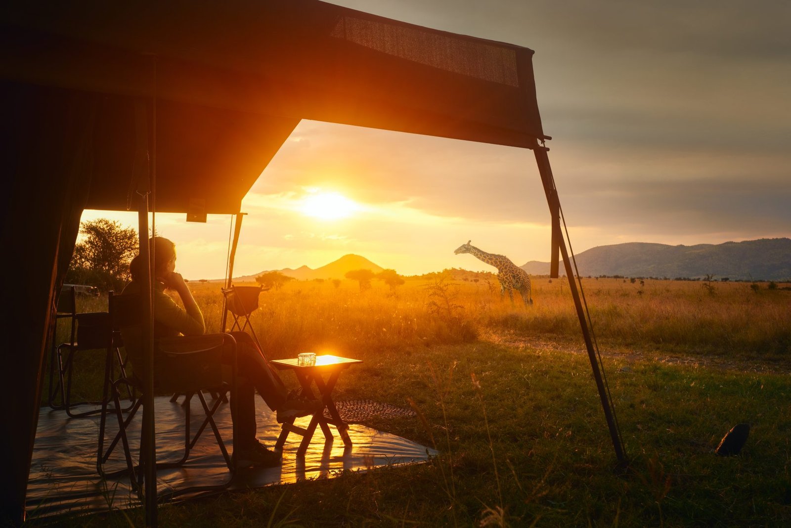 Guest at the edge of a luxury safari tent overlooking the savanna at sunset