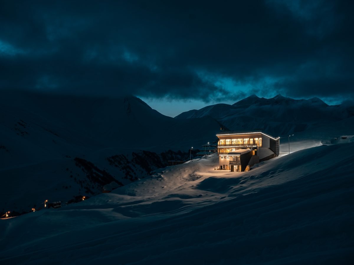 Lone alpine lodge glowing on a groomed dusk ski piste