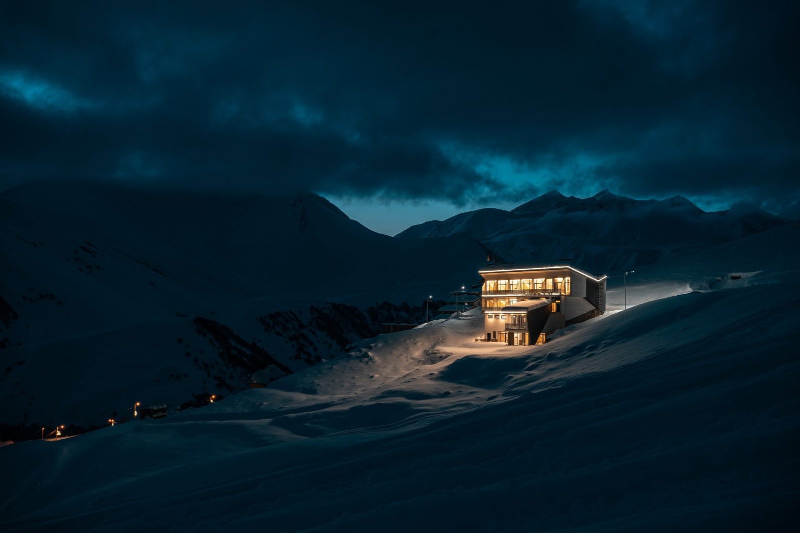 Lone alpine lodge glowing on a groomed dusk ski piste