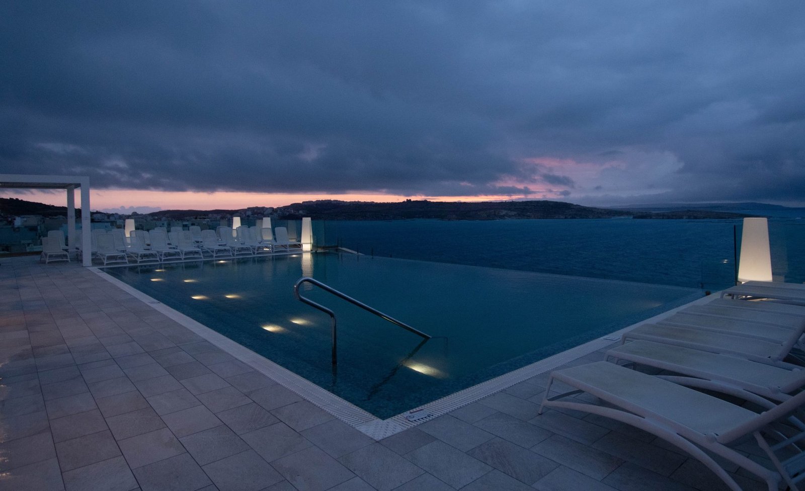 Rooftop infinity pool with lit canopy at blue dusk
