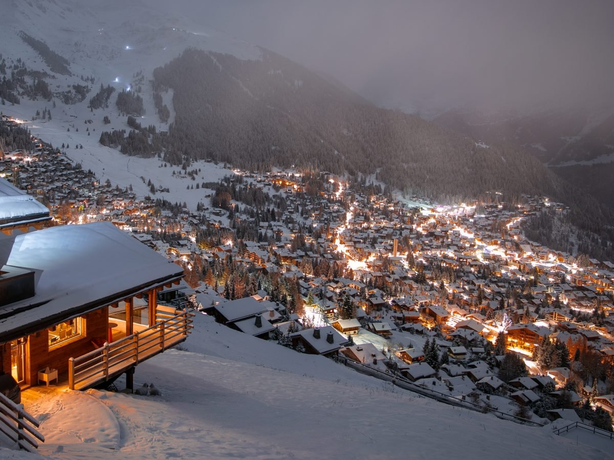 Chalet balcony above a valley of village lights in dusk snowfall