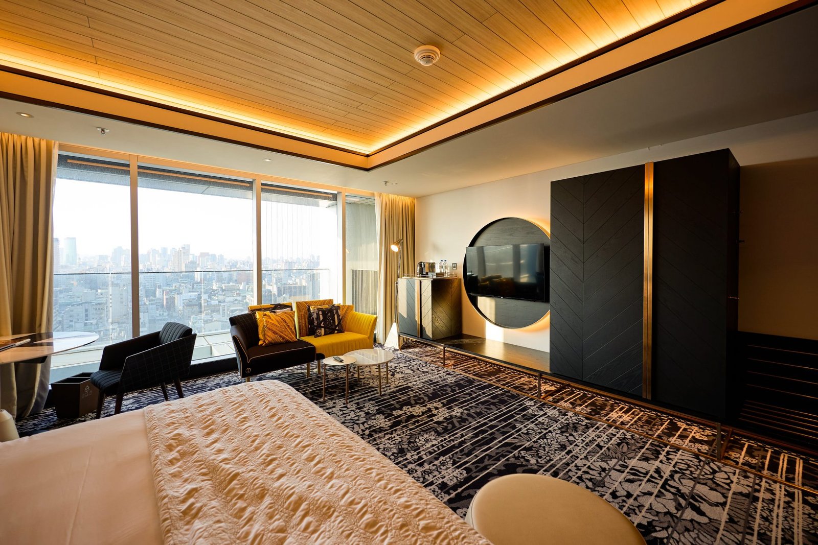 Modern hotel suite with a warm wood-lit ceiling and city view at dusk