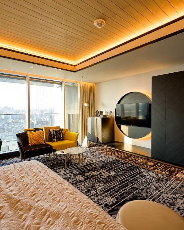Modern hotel suite with a warm wood-lit ceiling and city view at dusk