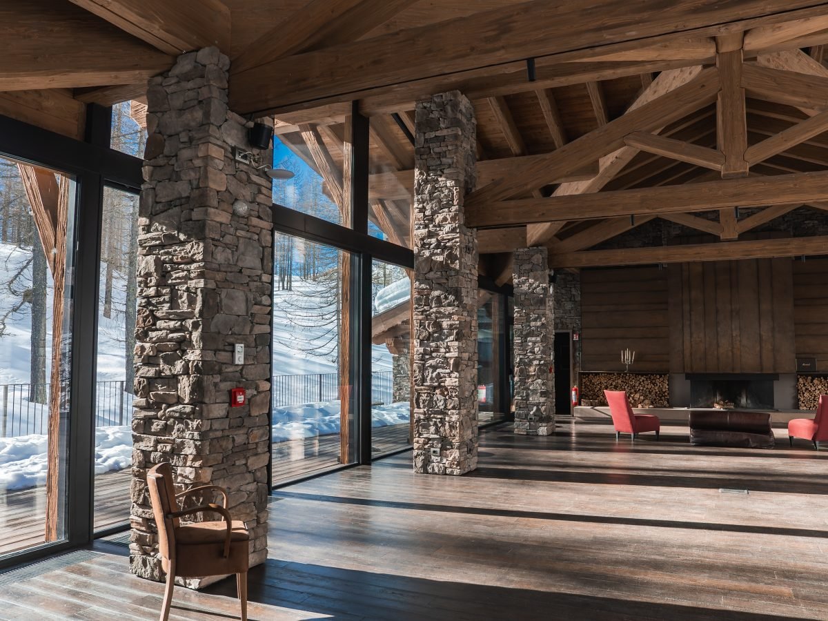 Rustic alpine chalet lounge with stone columns, fire and mountain view
