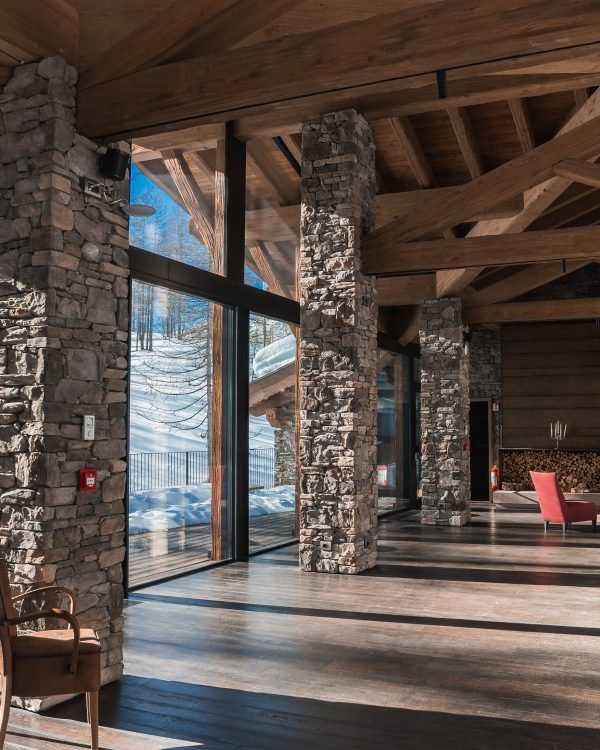 Rustic alpine chalet lounge with stone columns, fire and mountain view