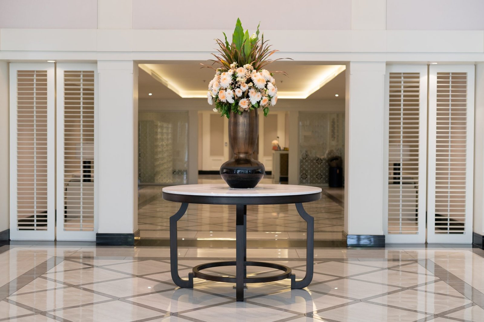 Symmetrical hotel foyer with a round marble table and flowers