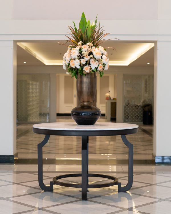 Symmetrical hotel foyer with a round marble table and flowers