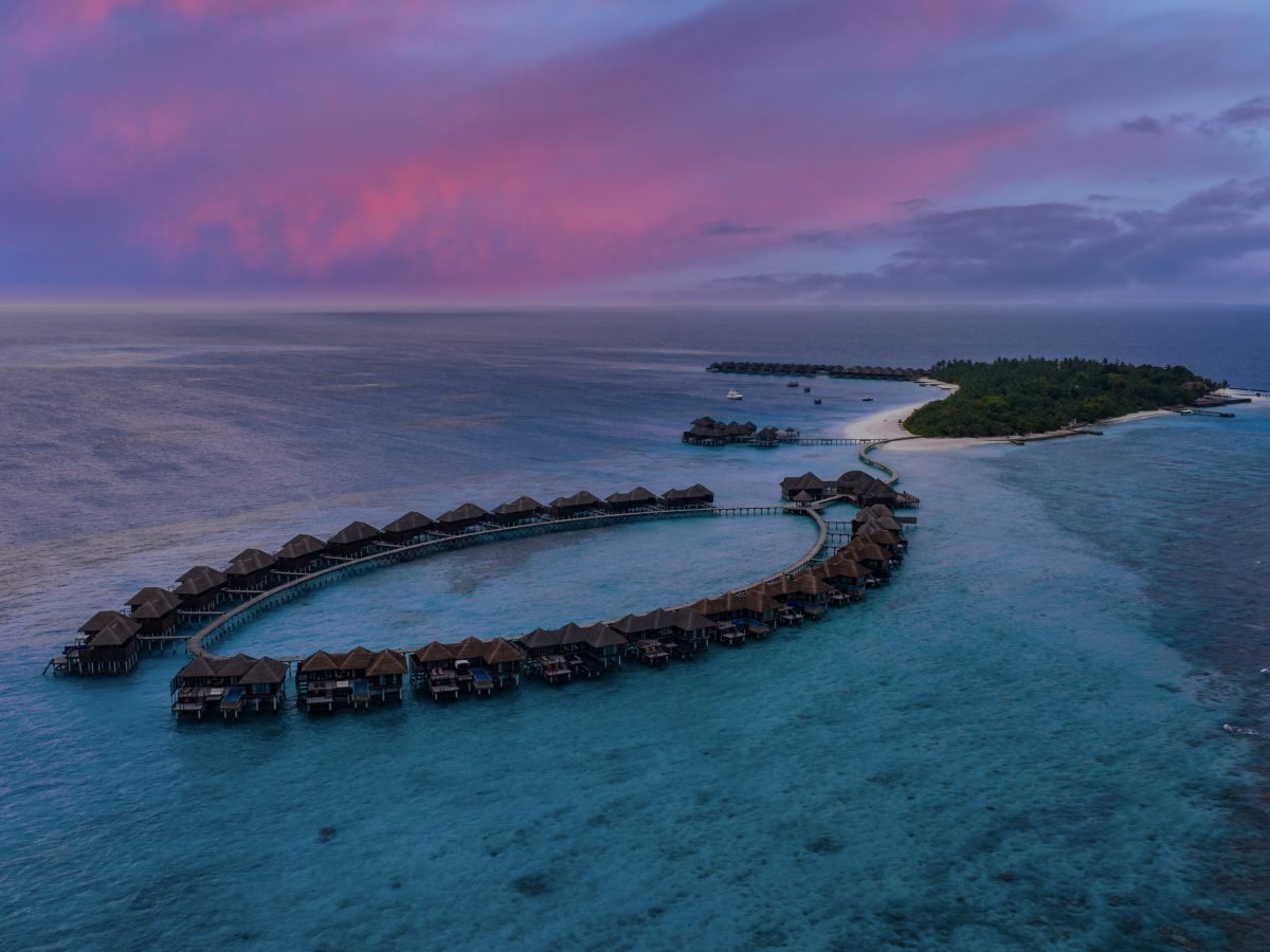 Aerial view of a Maldives overwater villa resort under a pink dusk sky