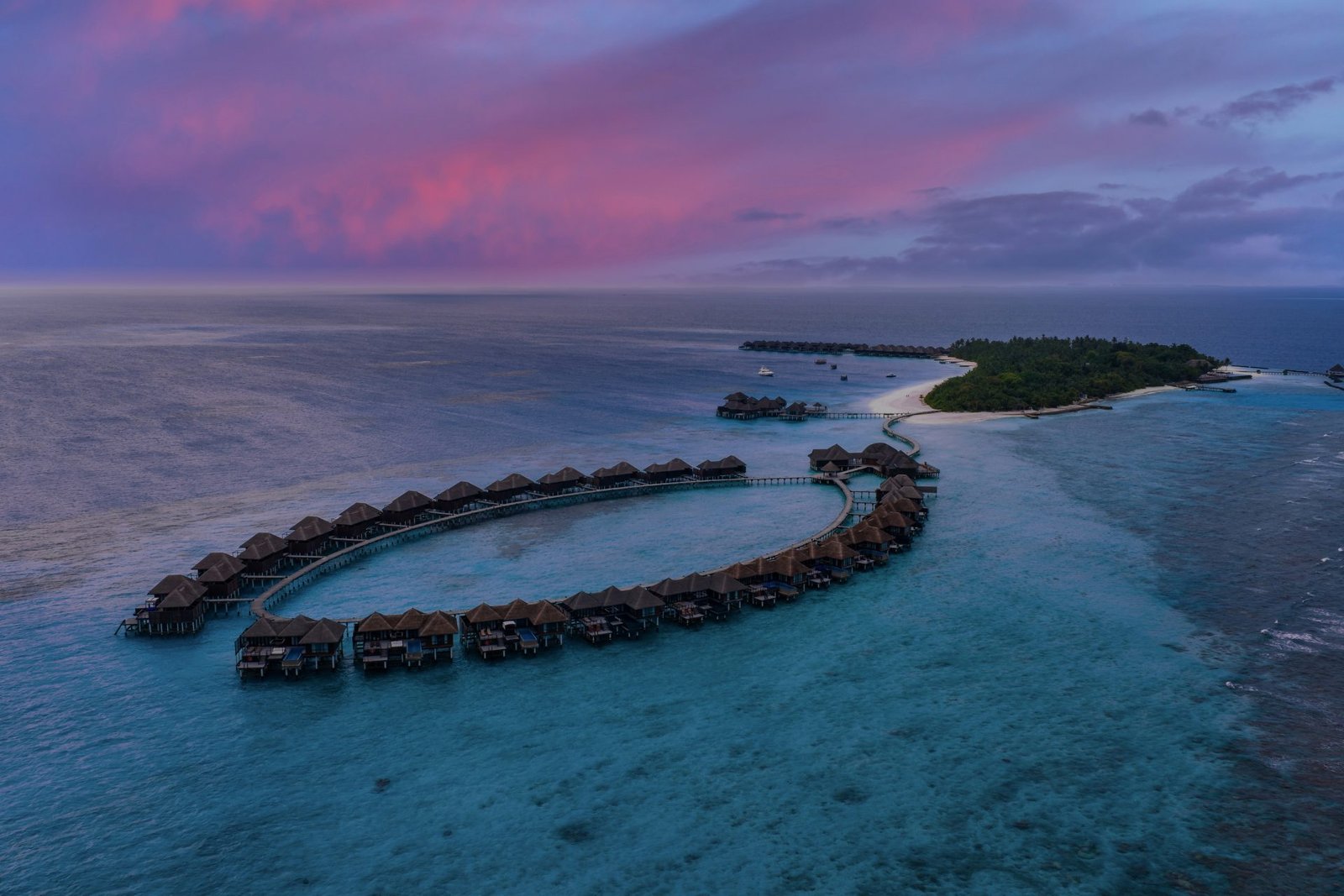 Aerial view of a Maldives overwater villa resort under a pink dusk sky