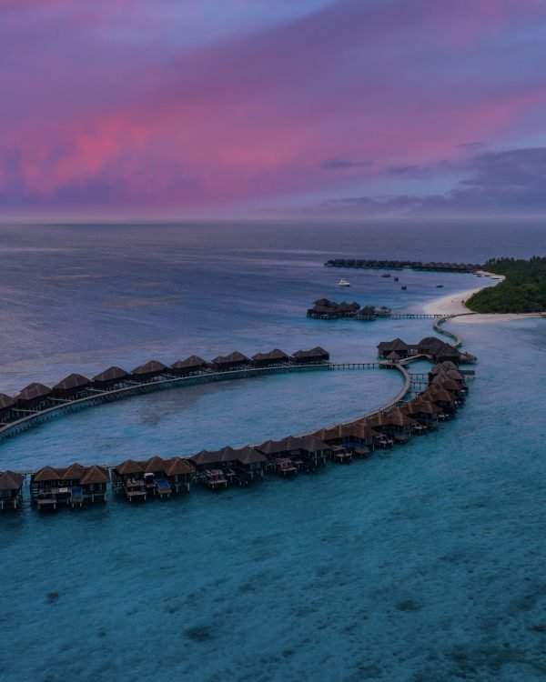 Aerial view of a Maldives overwater villa resort under a pink dusk sky