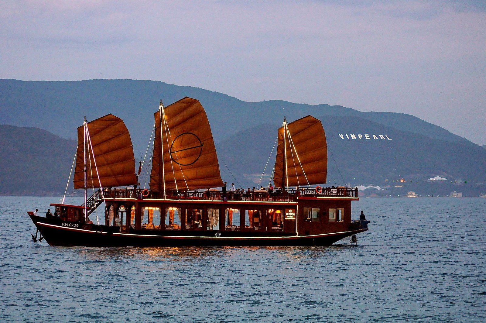 Emperor Cruises luxury wooden boat with traditional red sails cruising across calm water near Vinpearl in Vietnam.